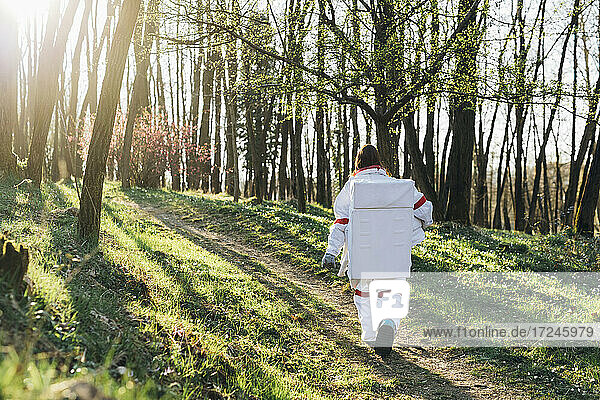 Female explorer wearing space suit walking on forest path
