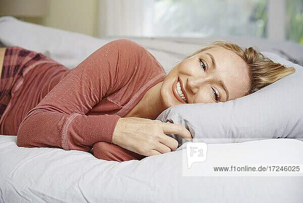 Lächelnde Frau auf dem Bett liegend im Schlafzimmer