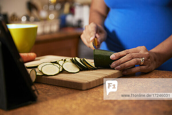 Frau schneidet Zucchini auf einem Holzbrett in der Küche