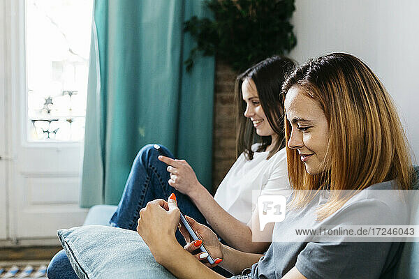 Schöne Frau  die ein Mobiltelefon benutzt  während sie bei ihrer Freundin zu Hause sitzt