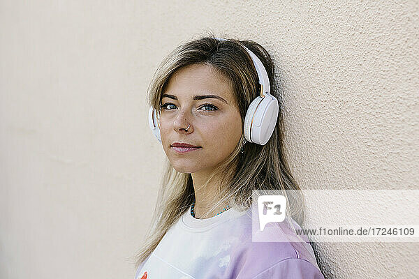 Frau mit Kopfhörern hört Musik  während sie sich an die Wand lehnt