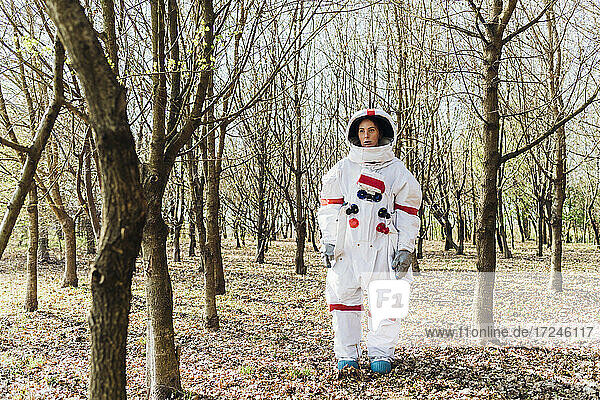 Young female astronaut in space contemplating while standing by bare tree in forest