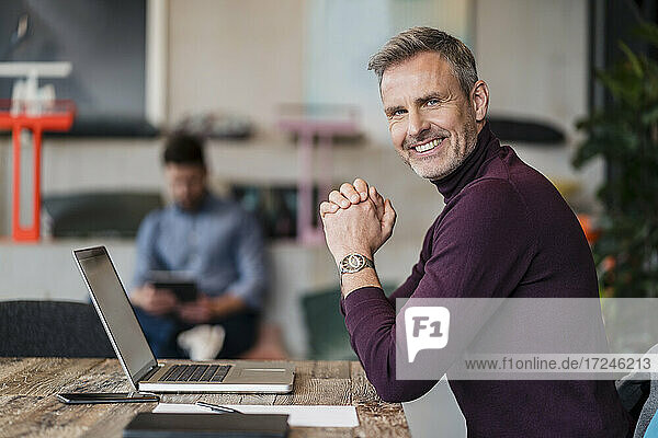 Reifer männlicher Unternehmer mit Laptop über Tisch am Arbeitsplatz