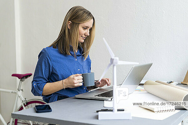 Geschäftsfrau hält Kaffeetasse und benutzt Laptop im Büro
