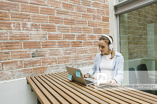 Weibliche Berufstätige mit Kopfhörern bei einem Videogespräch am Laptop in der Cafeteria