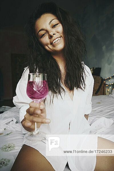 Hispanische Frau mit Weinglas im Schlafzimmer sitzend