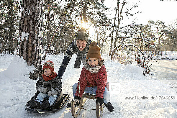 Father sledding with sons on snow during winter