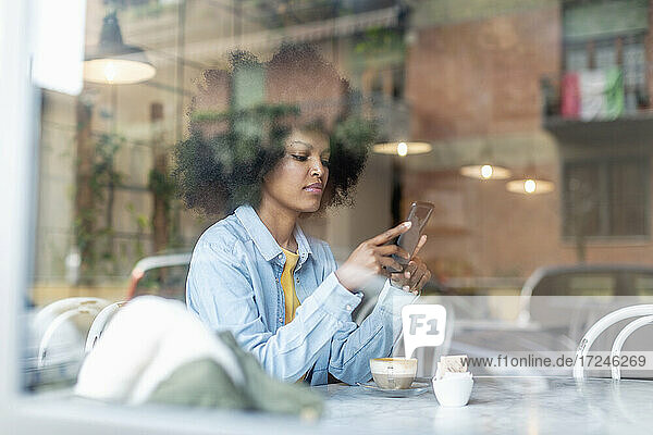 Weibliche Fachkraft  die ein Smartphone benutzt  sitzt in einem Café  gesehen durch Glas