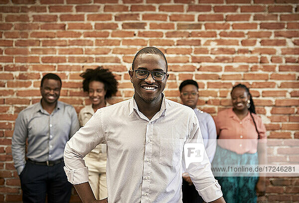 Lächelnder Geschäftsmann mit männlichen und weiblichen Kollegen  die im Hintergrund in einem Coworking-Büro stehen