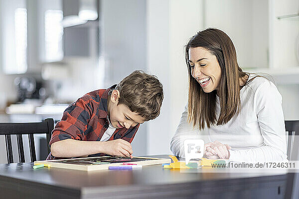 Smiling mother looking at son drawing on slate in kitchen