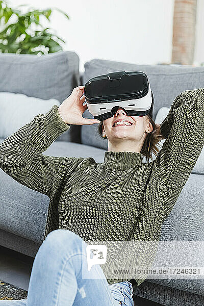 Lächelnde Frau im Pullover mit Virtual-Reality-Headset zu Hause