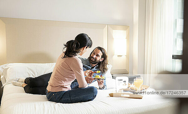 Smiling man looking at woman while having breakfast on bed