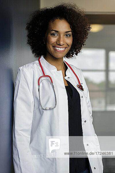 Smiling female doctor standing by wall in hospital