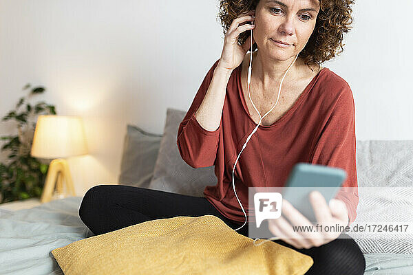 Frau  die ein Smartphone benutzt  während sie zu Hause über Kopfhörer Musik hört