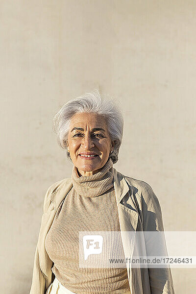 Lächelnde reife Frau vor einer Mauer an einem sonnigen Tag
