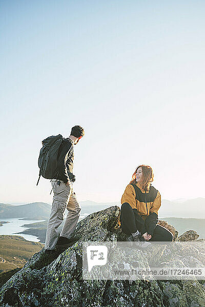 Junge Wanderin sitzt neben einem Mann  der auf dem Gipfel eines Berges steht