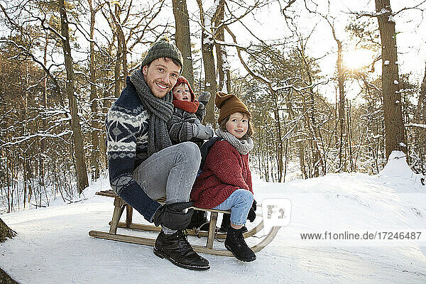 Father sitting on sled with sons during winter