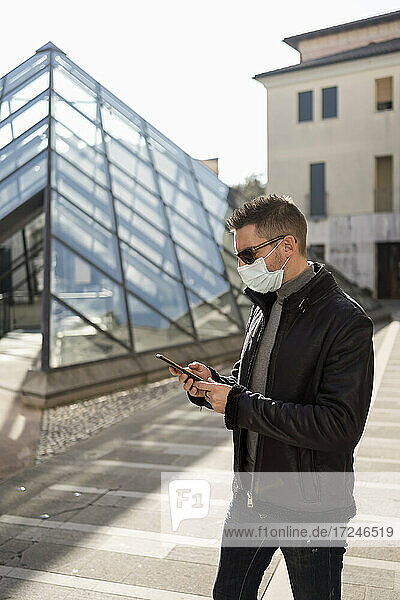 Mann mit Gesichtsmaske telefoniert während der Pandemie auf dem Fußweg