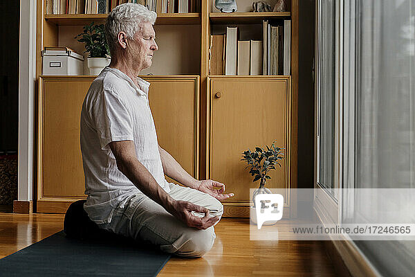 Mann übt Yoga  während er zu Hause im Lotussitz sitzt