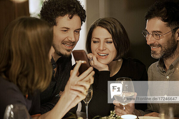 Reife Frau zeigt Handy an männliche und weibliche Freunde während einer Feier zu Hause
