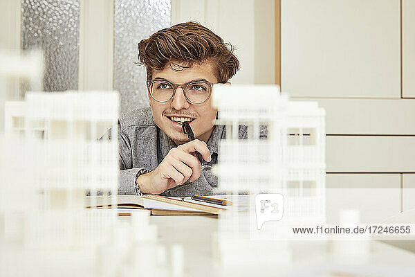 Thoughtful male architect smiling while looking away on table