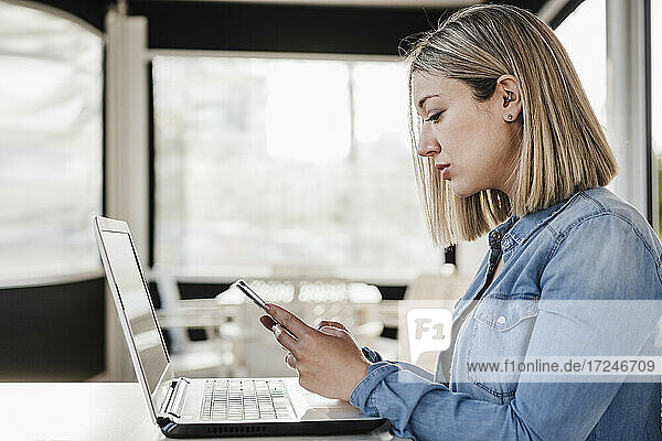 Geschäftsfrau mit Mobiltelefon vor einem Laptop in einem Café