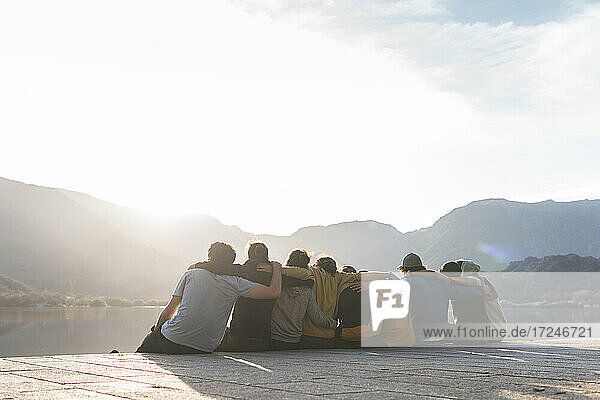 Männliche und weibliche Freunde  die an einem sonnigen Tag auf der Promenade sitzen und sich umarmen