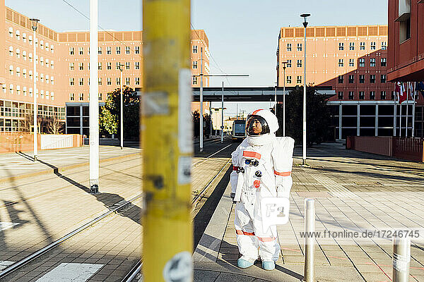Weibliche Astronautin schaut weg  während sie in der Nähe von Fahrgassen auf einem Fußweg in der Stadt steht