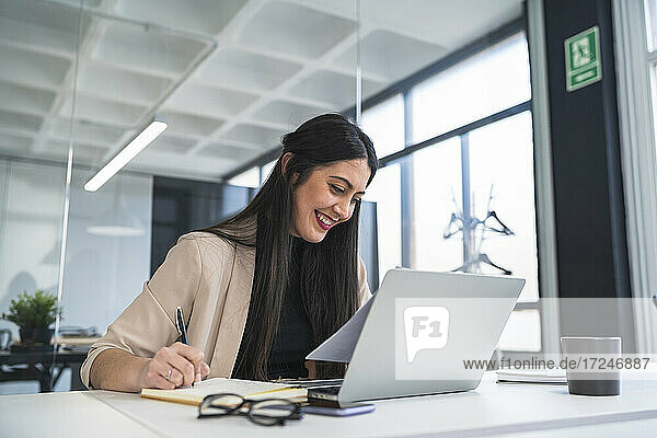 Lächelnde weibliche Fachkraft  die ein Dokument am Schreibtisch im Büro liest