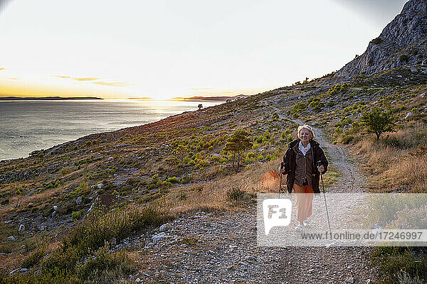 Senior woman with hiking poles on footpath near Adriatic sea in Omis  Dalmatia  Croatia