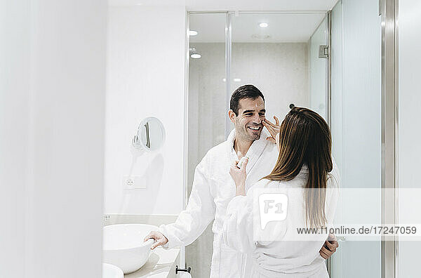 Eine Frau cremt das Gesicht eines Mannes ein  während sie in einem Hotelbad steht