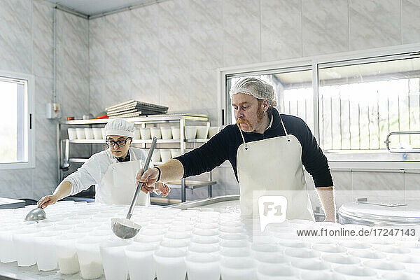 Geschultes Köchepaar bei der Herstellung von Käse in Containern in einer Fabrik