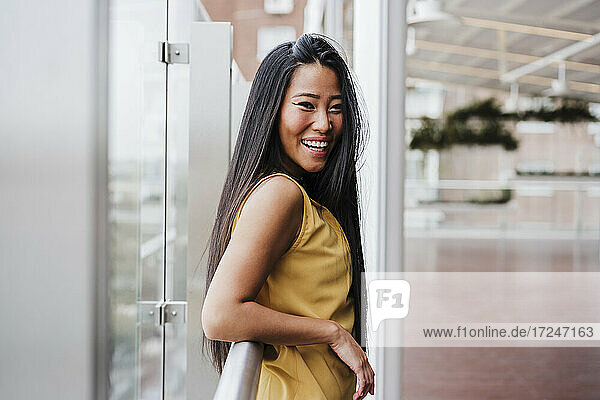 Cheerful businesswoman leaning on railing at modern office