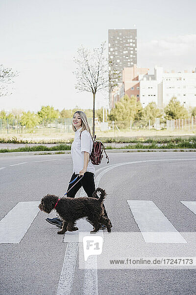 Lächelnde Frau mit Hund beim Überqueren der Straße in der Stadt