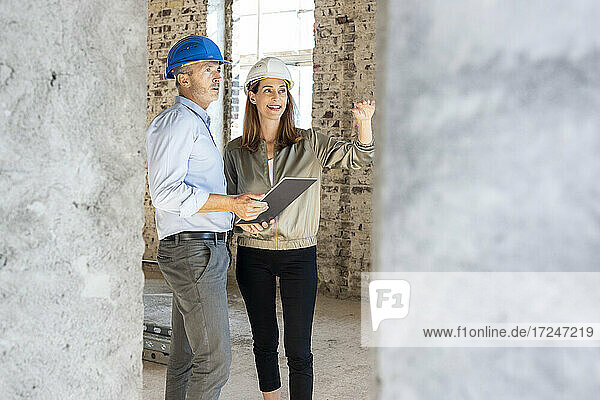 Weiblicher Bauherr gestikuliert bei der Diskussion mit einem männlichen Architekten auf der Baustelle