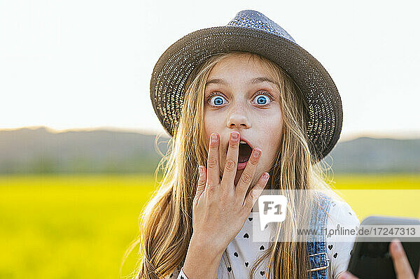 Schockiertes blondes Mädchen mit Hut auf einem landwirtschaftlichen Feld