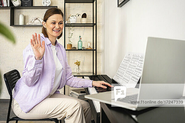 Lächelnde Frau winkt während eines Videogesprächs auf dem Laptop zu Hause