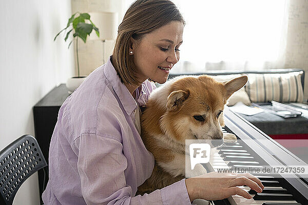Lächelnde Frau mit Hund spielt zu Hause Keyboard