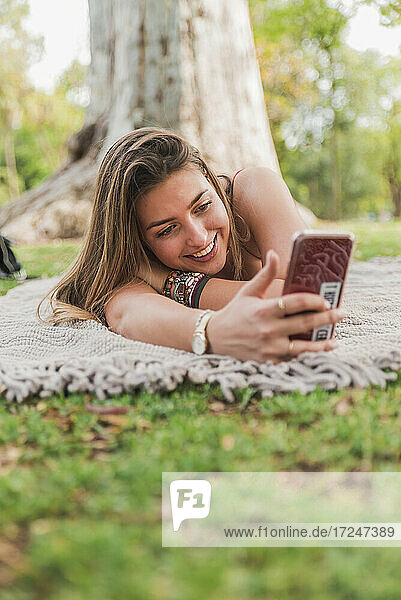 Smiling woman taking selfie through mobile phone in public park