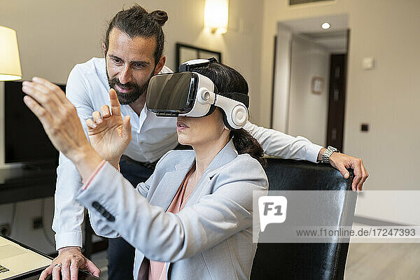Reife Geschäftsfrau trägt Virtual-Reality-Simulator von männlichem Kollegen im Hotel