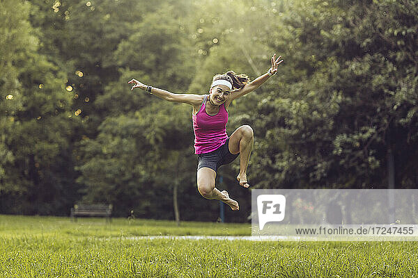Fröhliche Frau springt über Gras im Park