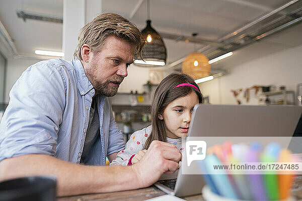 Mature man assisting girl e-learning through laptop at home