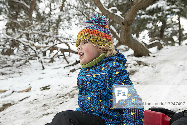 Curious boy looking away while sitting on snow during winter