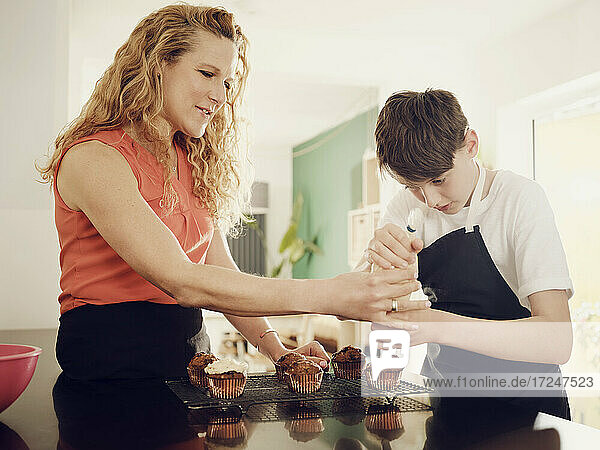 Mutter bringt ihrem Sohn bei  Muffins mit einem Spritzbeutel in der Küche zu Hause zu glasieren