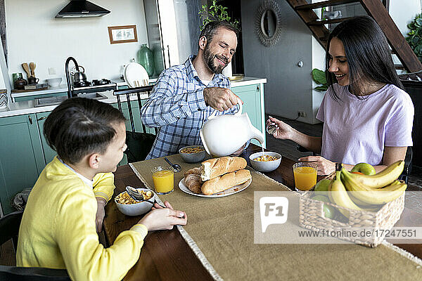 Father pouring milk while having breakfast with family at home