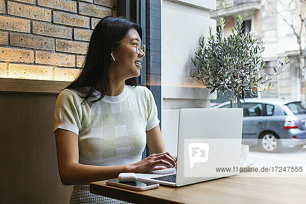 Nachdenkliche Frau schaut weg  während sie einen Laptop im Café benutzt