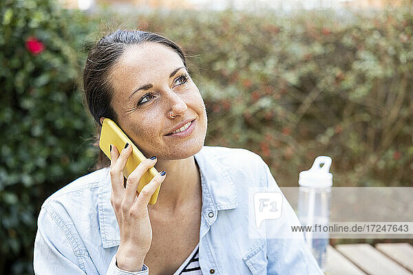 Lächelnde weibliche Fachkraft schaut weg  während sie im Garten telefoniert
