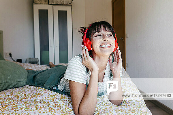 Schöne Frau mit Kopfhörern  die lächelnd auf dem Bett liegt