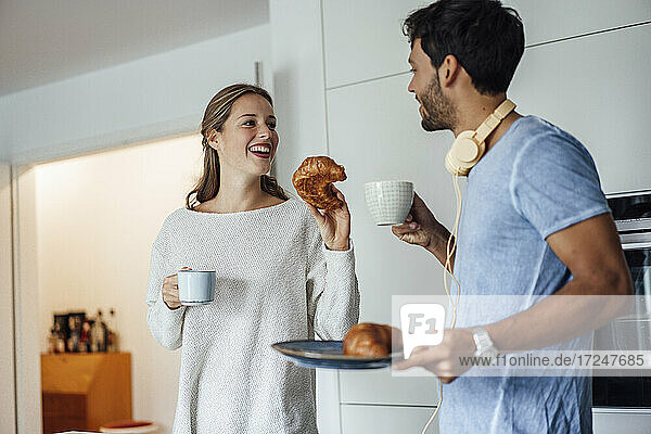 Happy young couple with croissant and coffee cup in kitchen