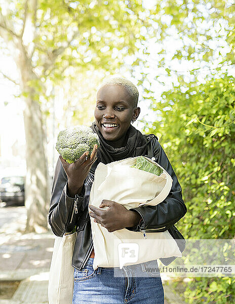 Short haired woman holding broccoli on footpath